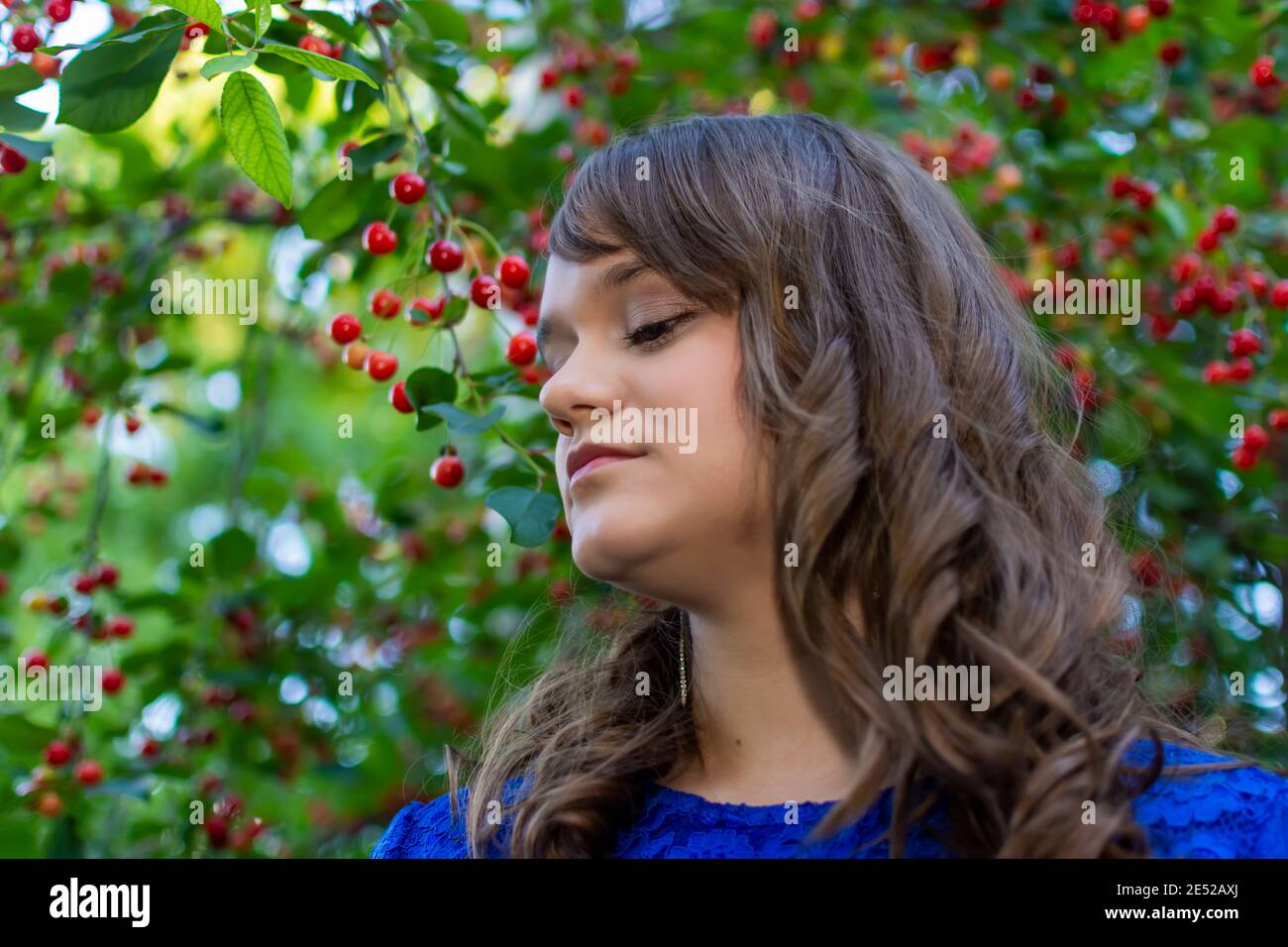 Jolie fille souriant en prenant des photos dans un jardin de cerises. Portrait de jeune fille avec maquillage. Fruits mûrs à l'arrière-plan. Représentant l'été Banque D'Images