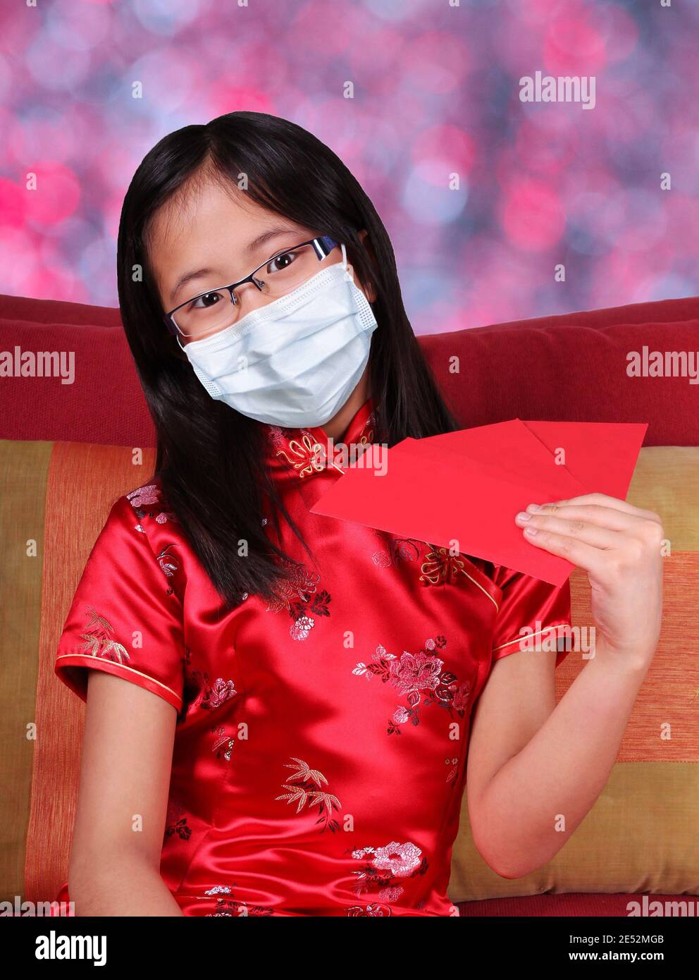 Célébrez le nouvel an chinois pendant la pandémie de Covid-19 avec une fille heureuse portant un masque et un cheongsam qipao traditionnel tenant des enveloppes d'argent rouge, un symb Banque D'Images