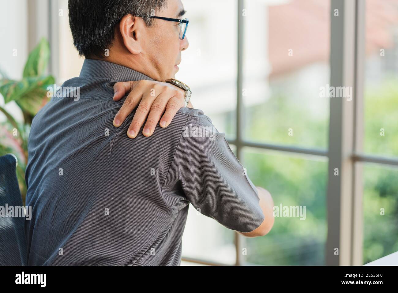 Un homme d'affaires asiatique expérimenté travaillant avec un ordinateur portable a un problème avec les douleurs d'épaule. Vieil homme qui ressent de la douleur après s'être assis longtemps à son bureau, Hea Banque D'Images