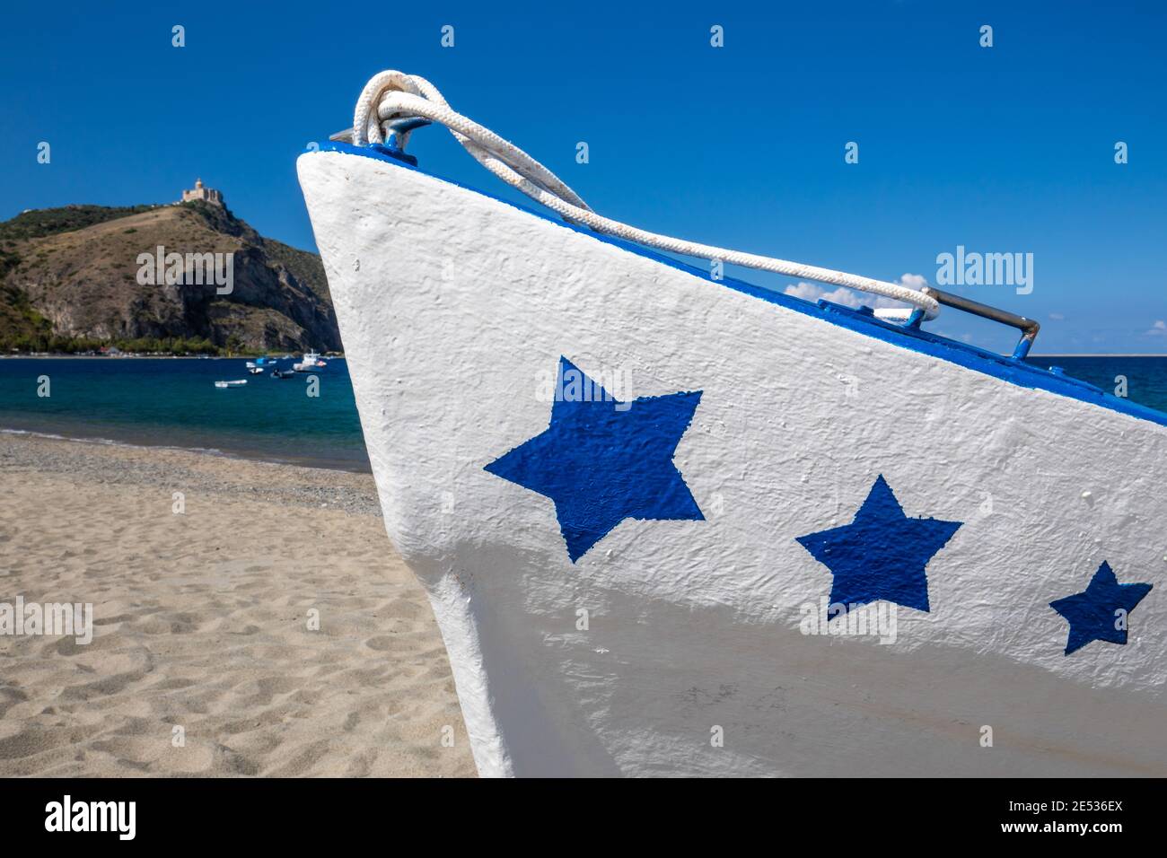 Gros plan d'un bateau de pêche blanc et bleu décoré d'étoiles sur sa prow, allongé à terre sur une plage de sable en une journée ensoleillée d'été Banque D'Images