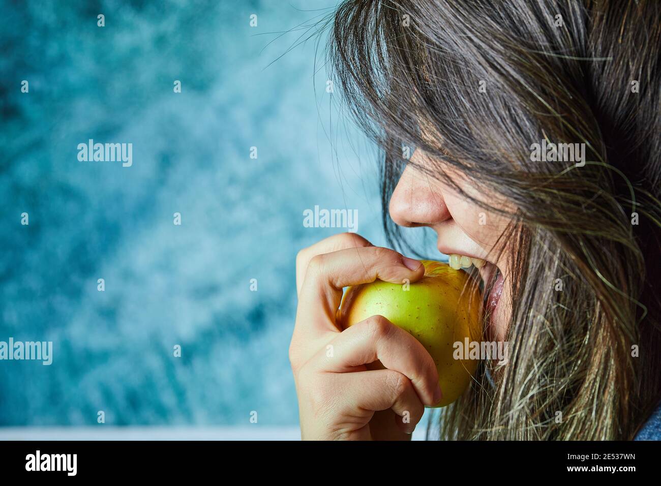 Femme mangeant de la pomme sur fond bleu Banque D'Images