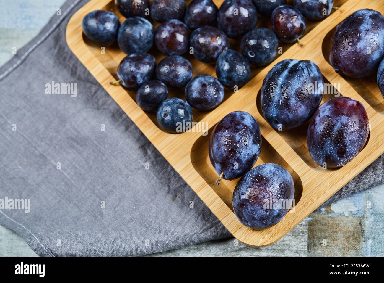 Prunes de jardin sur plateau en bois avec nappe grise Banque D'Images