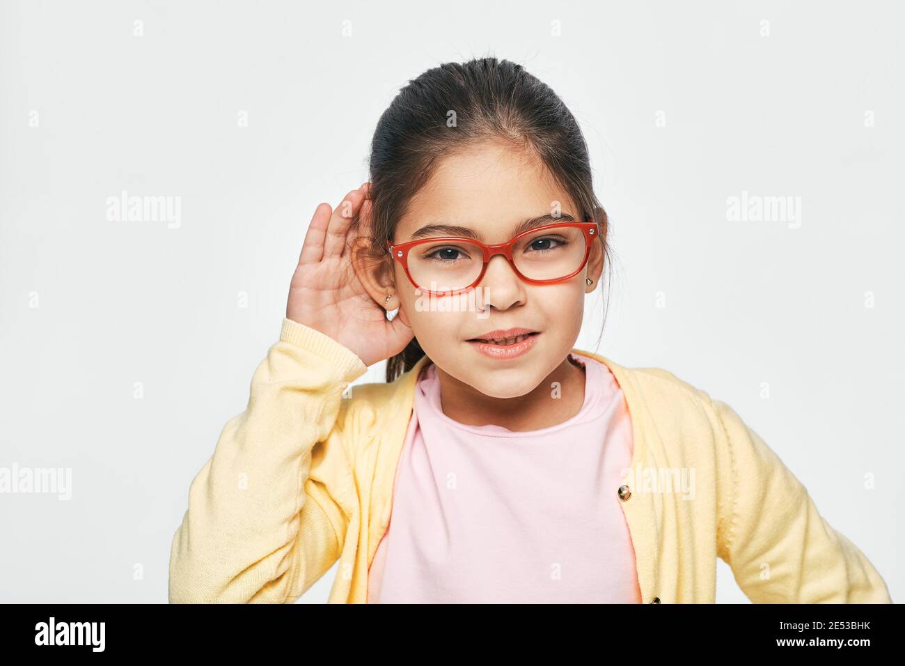 Race mixte petite fille tient la main près de son oreille pour écouter, isolé sur fond blanc. Concept de test auditif pour enfants Banque D'Images