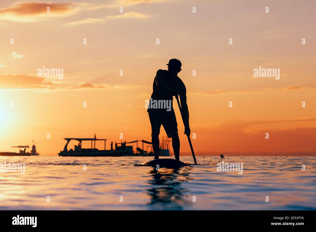 La palette active boarder. Coucher du soleil noir silhouette de jeune sportsman paddling on stand up paddleboard. Mode de vie sain. Sport d'eau, surf SUP Banque D'Images