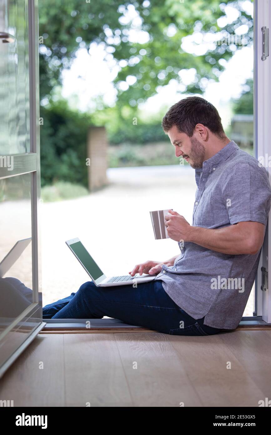 Homme d'affaires travaillant à la maison sur un ordinateur portable pendant une séance de verrouillage en cas de pandémie Dans la porte avant ouverte Banque D'Images