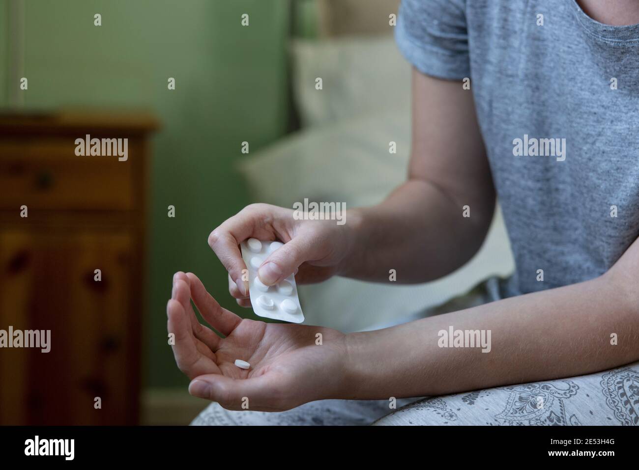 Gros plan d'une femme assise sur un lit portant un pyjama Médicament provenant d'un paquet de pilules Banque D'Images