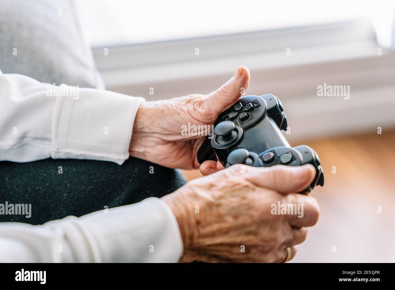 Crop anonyme 90 ans femme assis sur le canapé avec contrôleur moderne et jeux vidéo à la maison Banque D'Images