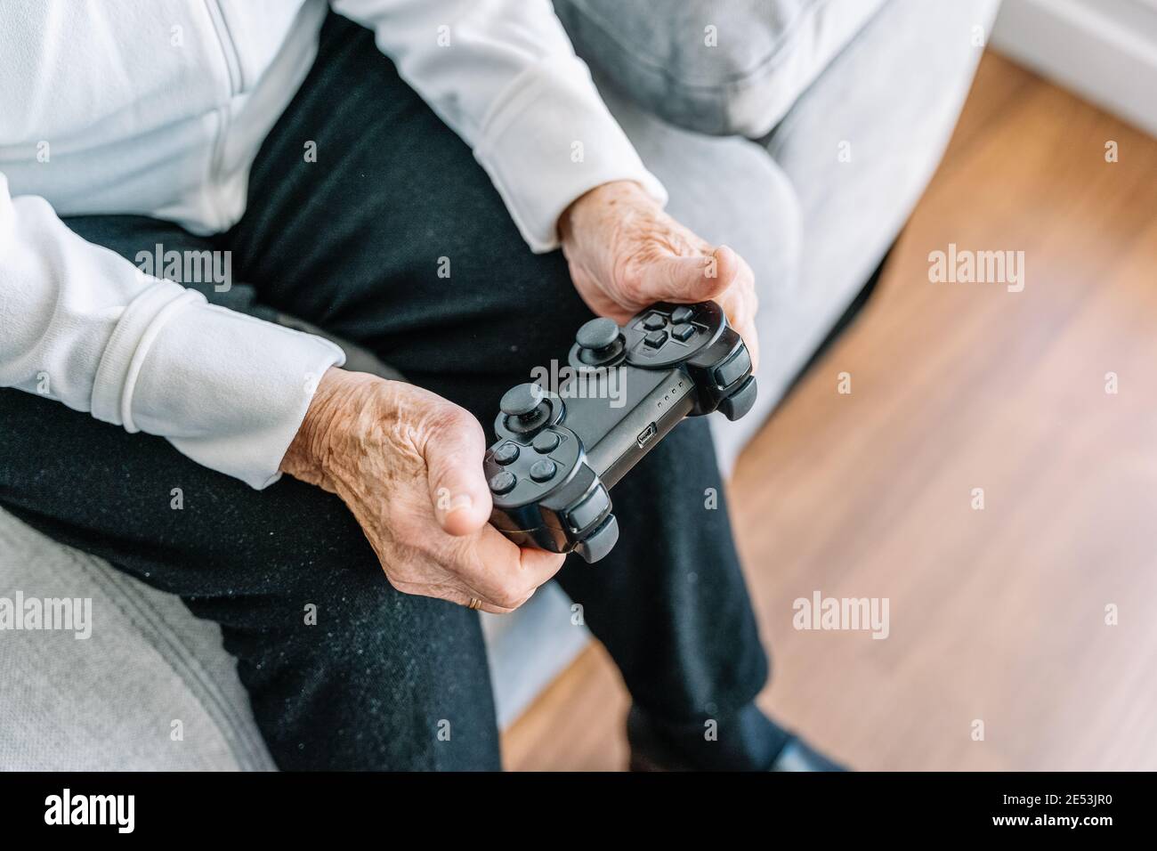 Crop anonyme 90 ans femme assis sur le canapé avec contrôleur moderne et jeux vidéo à la maison Banque D'Images