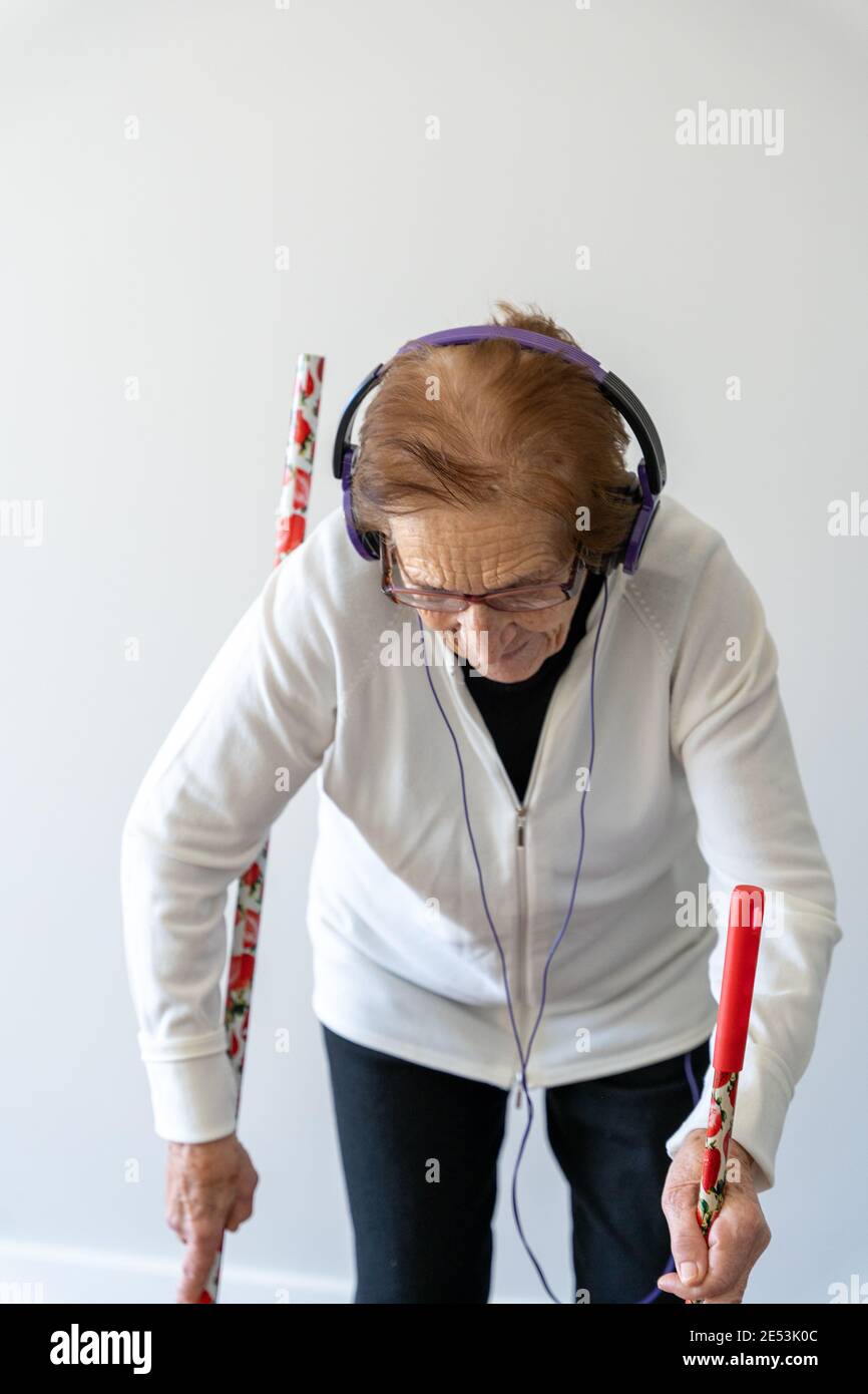 Joyeuse femme de 90 ans qui écoute de la musique dans un casque pendant balayer le sol avec un balai et faire des travaux ménagers Banque D'Images