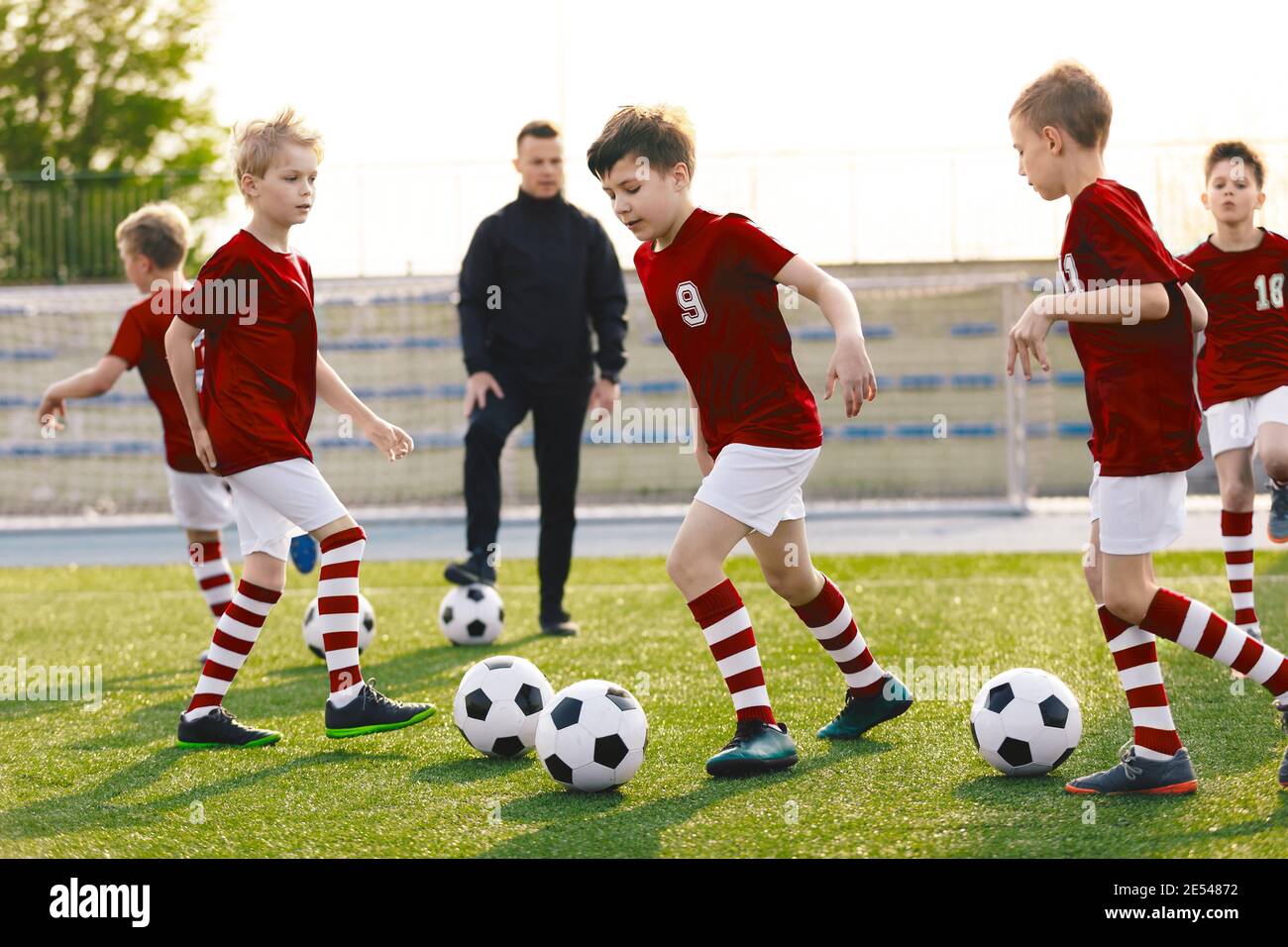Boys in Soccer Jersey kits Kicking Soccer balles sur la session d'entraînement. Jeune entraîneur de football école d'enseignement pour enfants. Balles de course pour enfants sur Grass Stadiu Banque D'Images