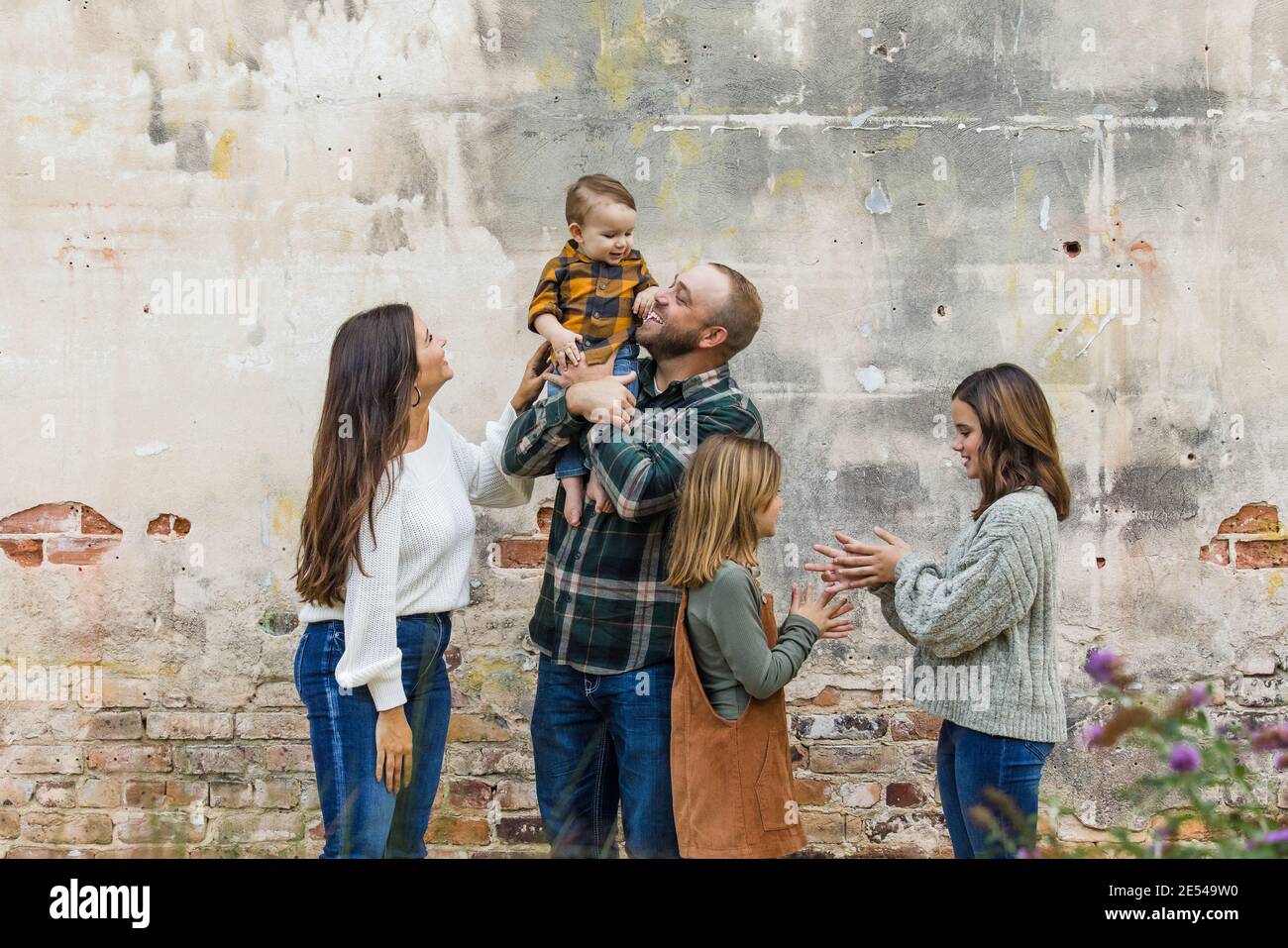 Une famille de cinq avec deux filles et un bébé garçon debout près d'un vieux mur de briques urbain Banque D'Images