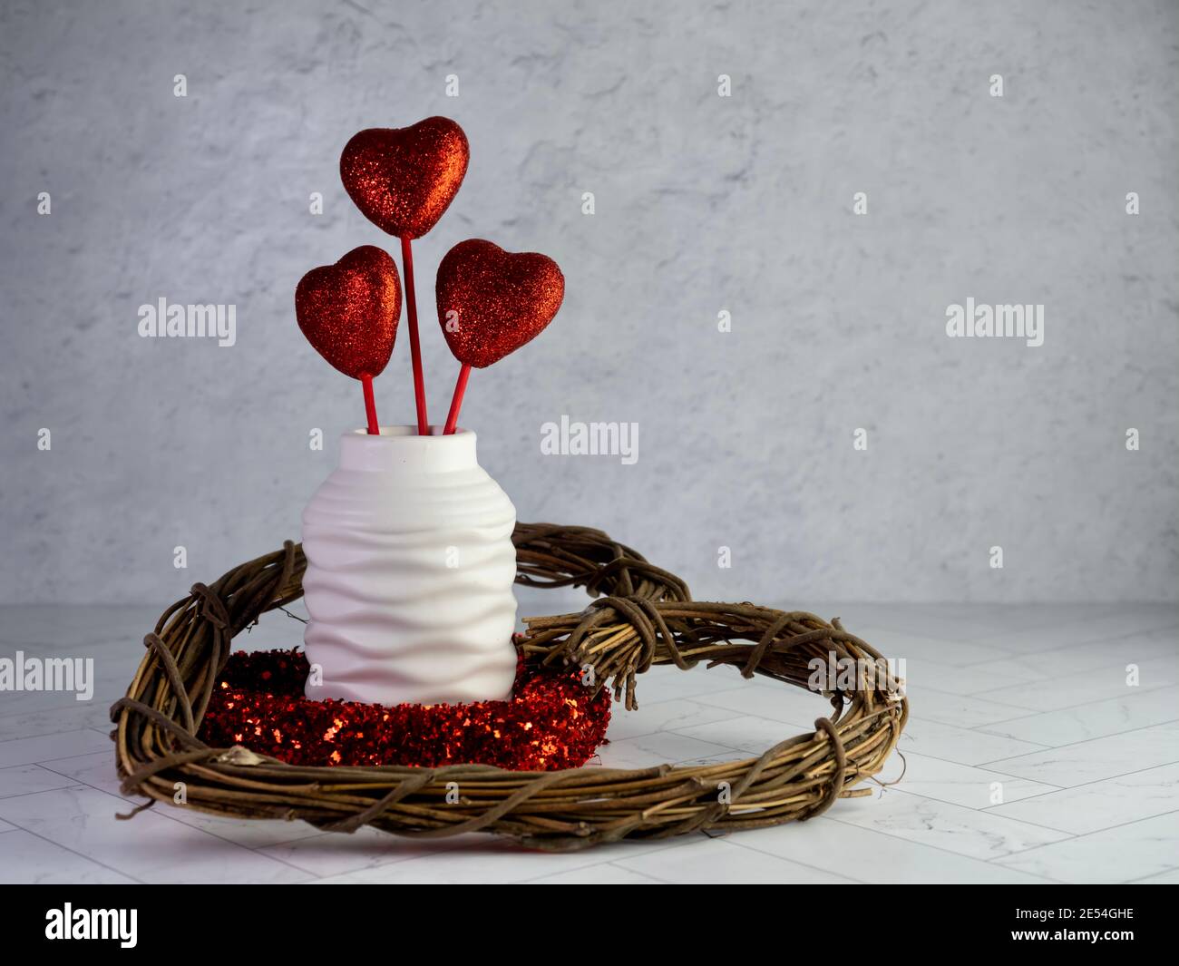 Décoration de Saint-Valentin, couronne en bois à coeur, couronne en coeur brillant rouge et vase blanc rempli de 3 coeurs brillants rouges collés sur un cerringbon Banque D'Images