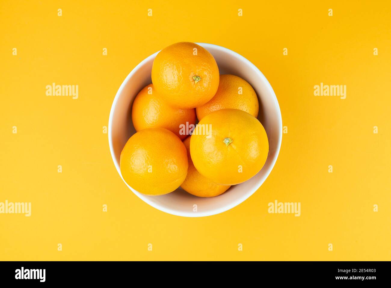 directement au-dessus de la vue d'un bol blanc rempli d'oranges juteuses sur fond orange Banque D'Images