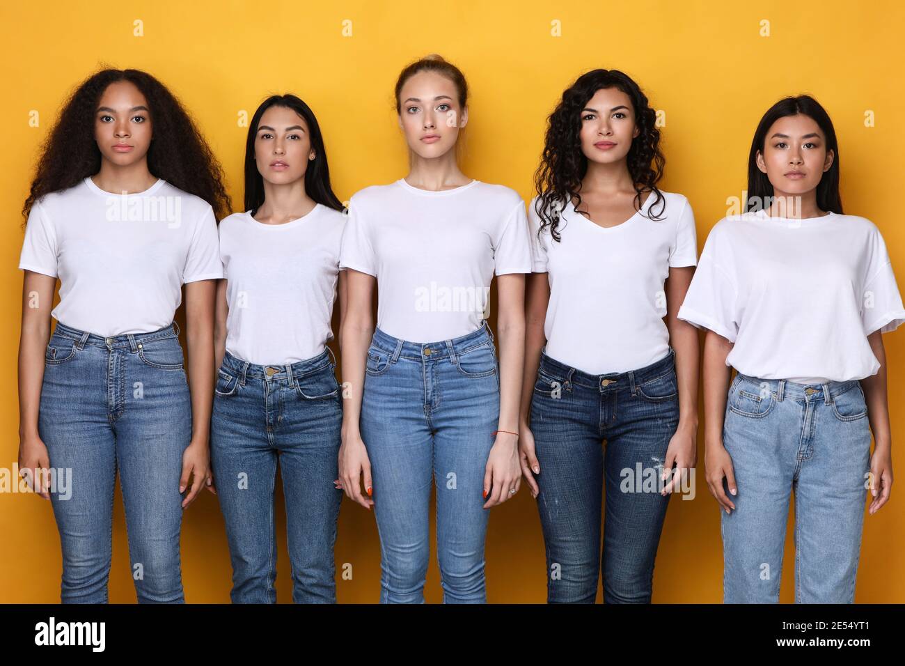 Groupe de cinq femmes multiraciales sérieuses debout sur fond jaune Banque D'Images