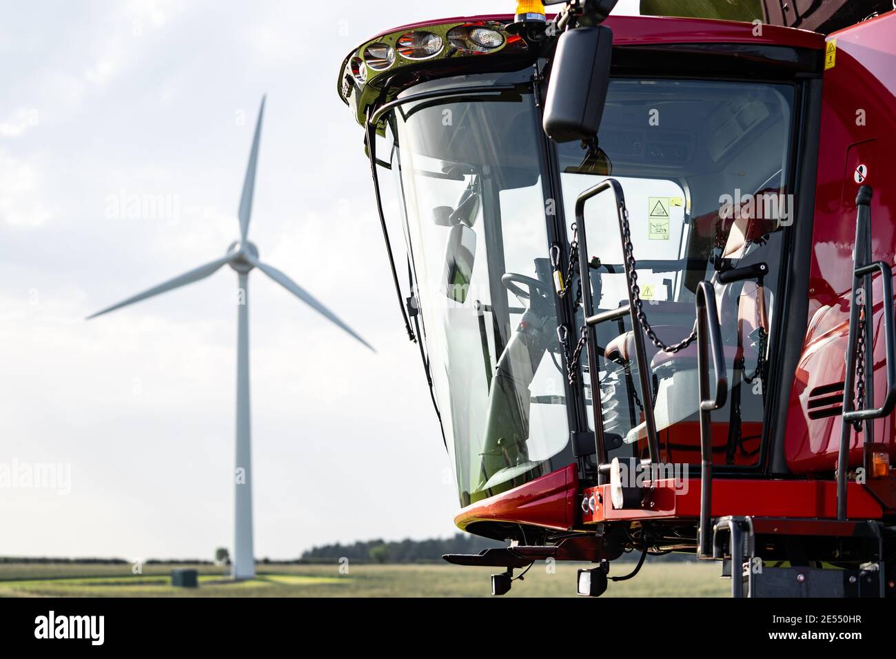 Gros plan sur les machines agricoles de la moissonneuse-batteuse rouge, sur la cabine du conducteur avec éolienne en arrière-plan sur les champs de ferme arbres réflexions d'herbe Banque D'Images