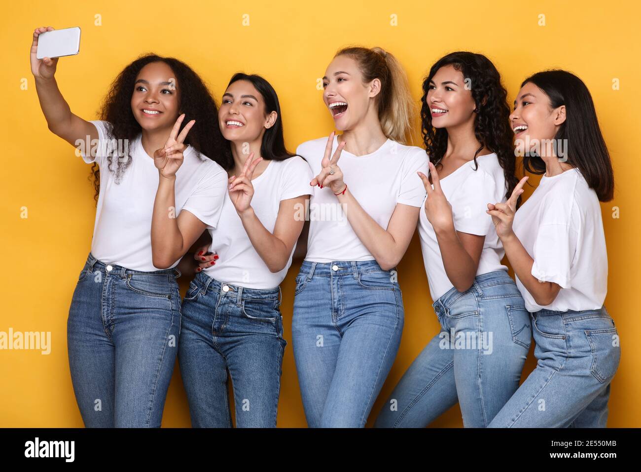 Multiculturel Dames faire Selfie au téléphone gestante V-Sign, fond jaune Banque D'Images