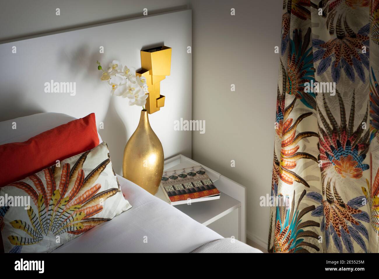 Lit avec table de chevet et vase doré avec orchidée, oreillers pour livres  et rideaux colorés, mur blanc avec lampe de créateur dorée Photo Stock -  Alamy