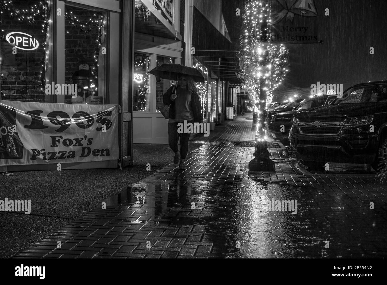 Prattville, Alabama/USA - 20 décembre 2018 : une femme marche le long d'un trottoir éclairé de façon festive devant Fox's Pizza sur main Street lors d'une nuit de pluie. Banque D'Images