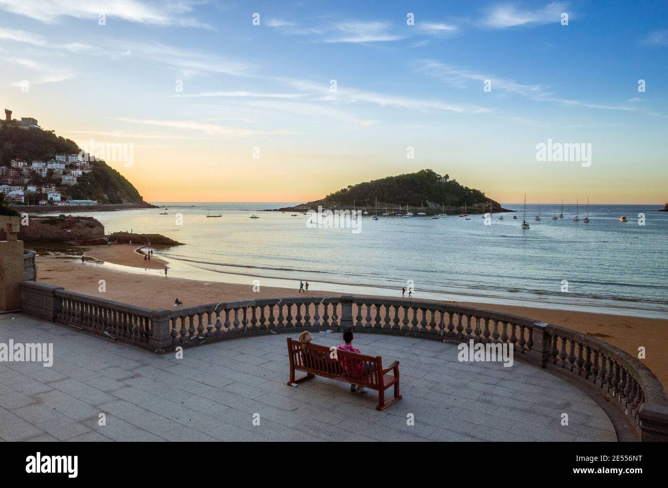 Donostia, Gipuzkoa, pays Basque, Espagne - 12 juillet 2019 : les gens s'assoient sur un banc pour admirer le coucher du soleil sur la plage de la Concha. Banque D'Images