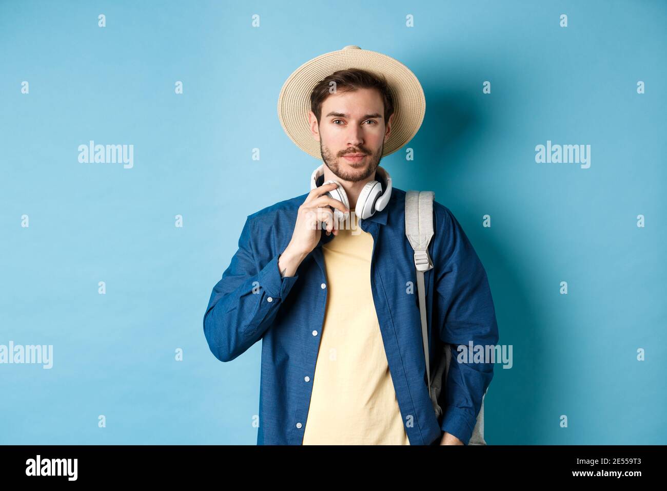 Beau gars voyageant avec un casque, portant un chapeau de paille et  souriant, debout avec un sac à dos sur fond bleu Photo Stock - Alamy