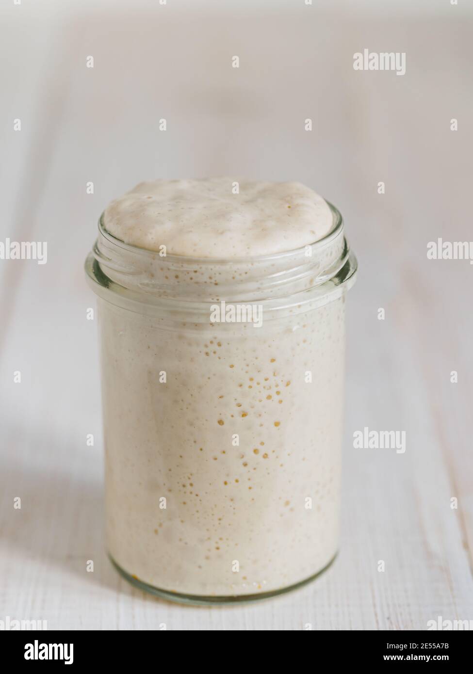 Démarreur de levain de blé. Bol en verre avec base de levain sur table en bois blanc. Copier l'espace pour le texte ou la conception. Verticale. Banque D'Images