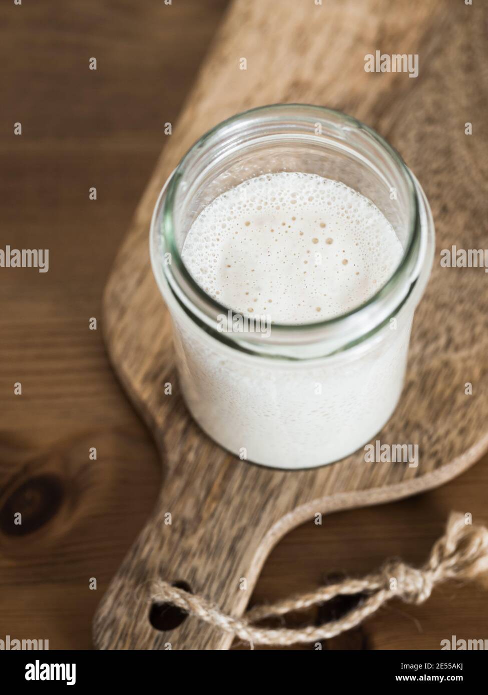 Démarreur de levain de blé. Bol en verre avec base de levain sur planche à découper en bois sur table en bois. Copier l'espace pour le texte ou la conception. Verticale. Banque D'Images