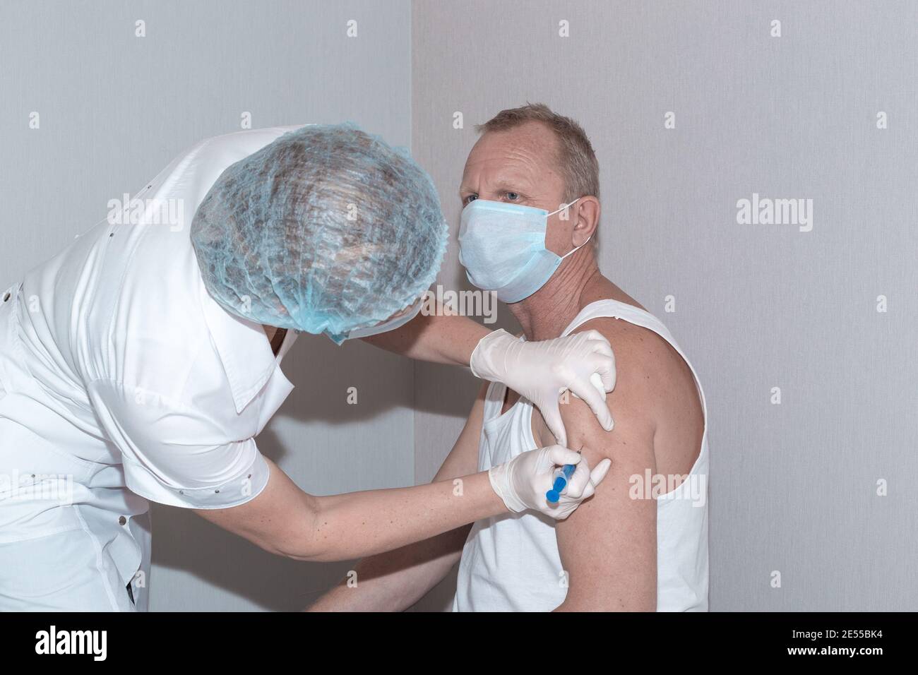 Vaccination contre le coronavirus. Une infirmière met le coup de feu dans l'épaule d'un homme mature portant un masque de protection. Immunisation de la population. Banque D'Images