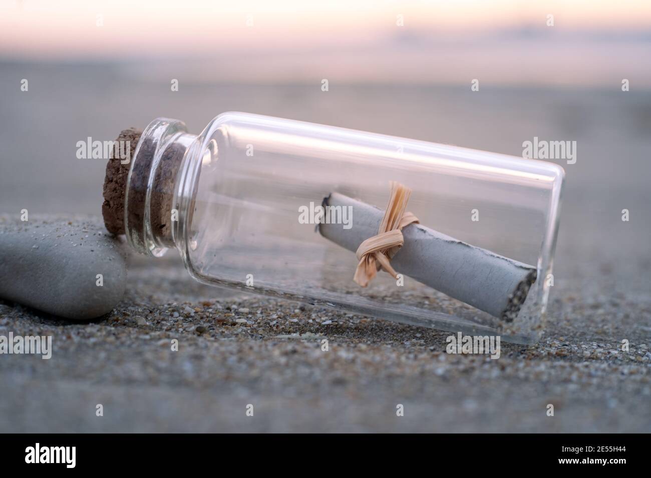 vue rapprochée d'une petite bouteille en verre contenant un message papier. La bouteille est posée sur la plage au lever du soleil. Banque D'Images