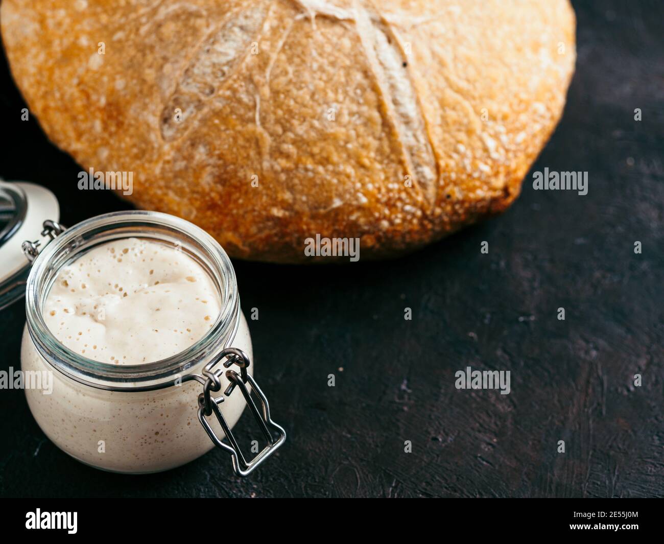 Pain de base Sourdoug et pain de levain de blé. Entrée de pâte aigre de blé dans un pot en verre et délicieux pain de pâte à pain rond maison sur fond noir, espace de copie. Concept de fabrication de pain au levain fait maison Banque D'Images