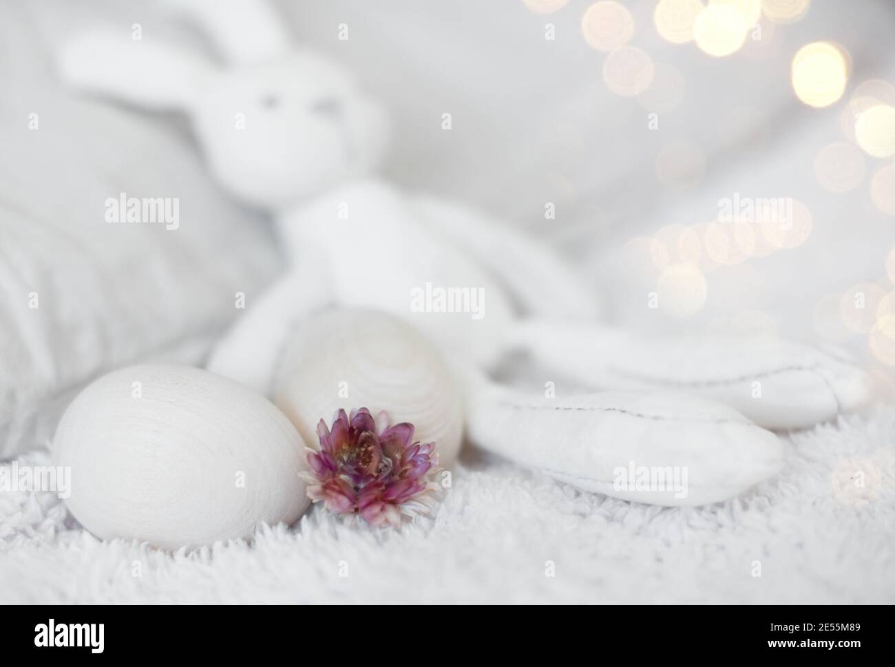 Pâques drôle blanc peluche lapin jouet sur un lit blanc avec des oeufs en bois zéro ouest. Banque D'Images