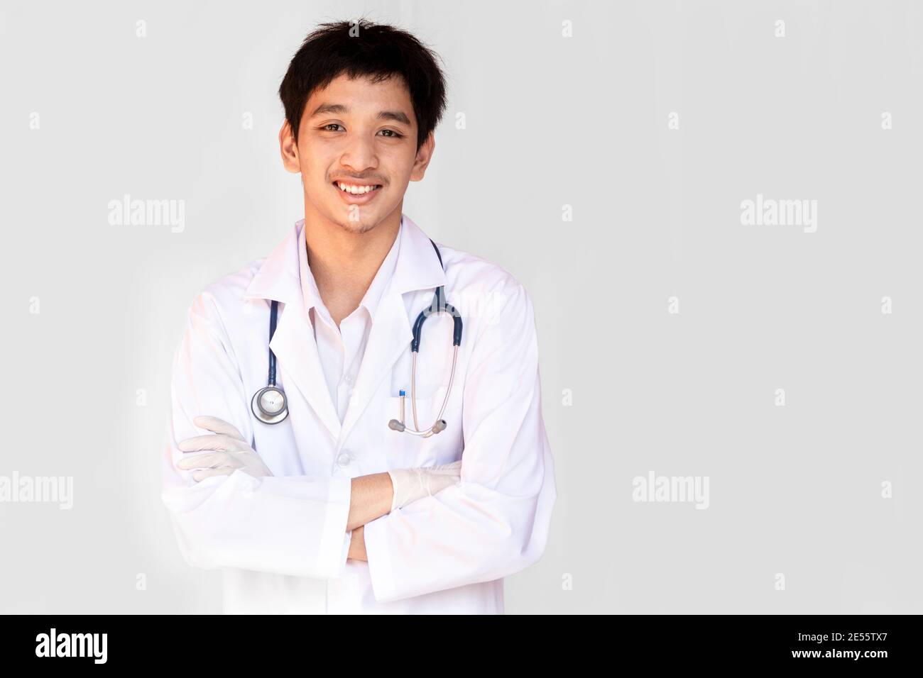 Un médecin souriant posant avec les bras croisés sur un fond blanc porte un stéthoscope. Jeune médecin asiatique portant un manteau blanc. Banque D'Images