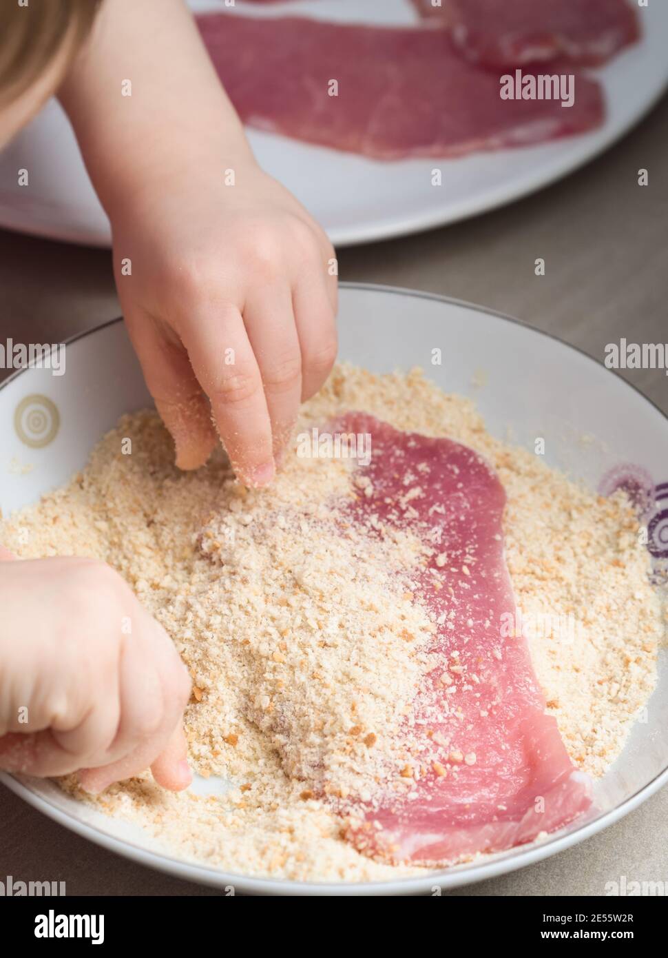 Enfant couvrant la viande de porc avec de la chapelure dans la cuisine Banque D'Images