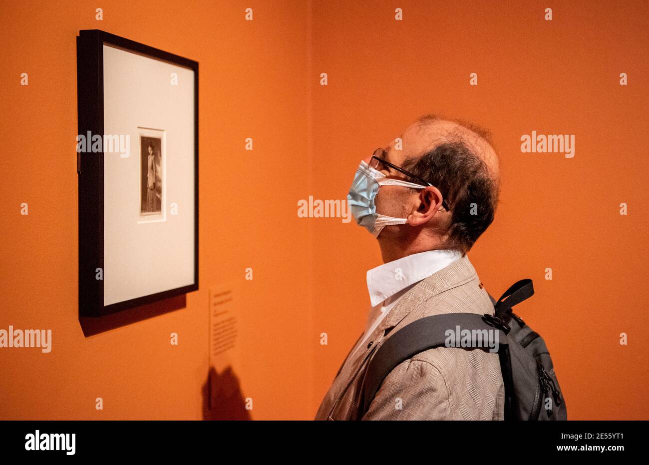 Un homme portant une couverture de visage regarde un dessin d'Aubrey Beardsley sur un fond orange vif. Banque D'Images