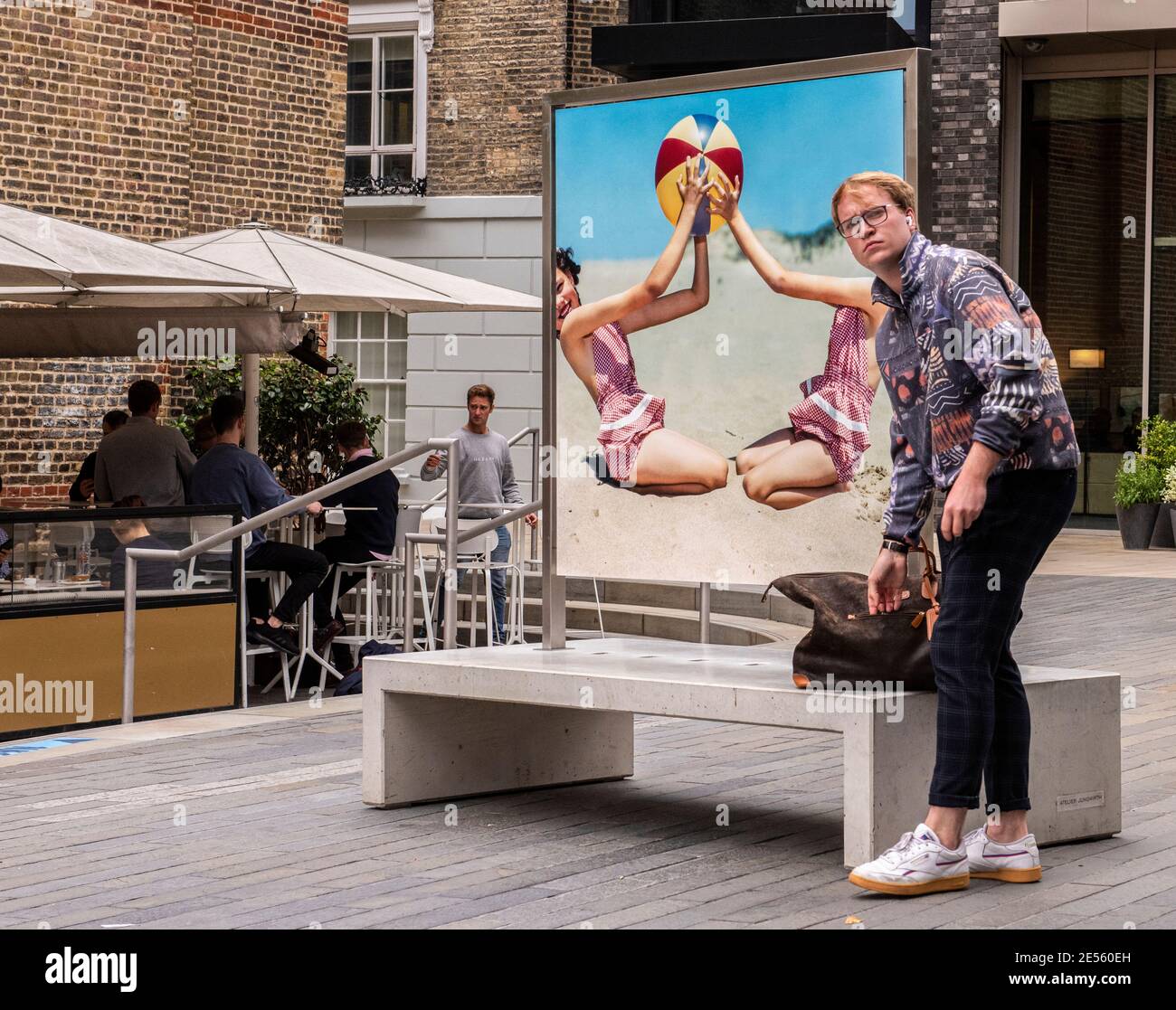 Jeune homme debout par une affiche rétro semble confus près de Kings Cross. Banque D'Images