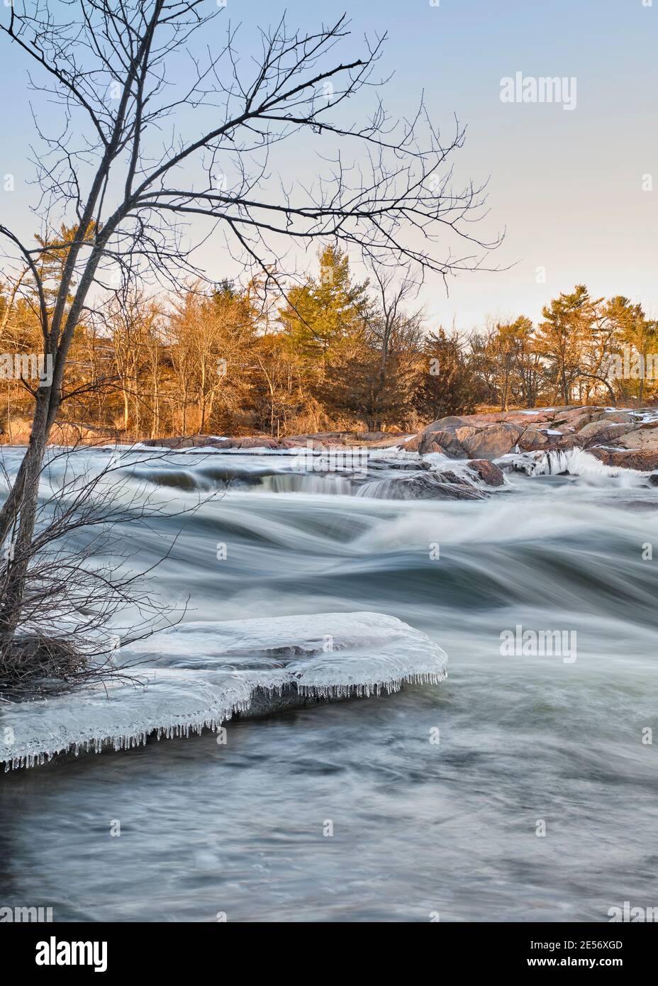 Le lever du soleil illumine les arbres et les rochers en granit des chutes Burleigh tandis que de la glace se forme sur les rives au début de l'hiver. Banque D'Images