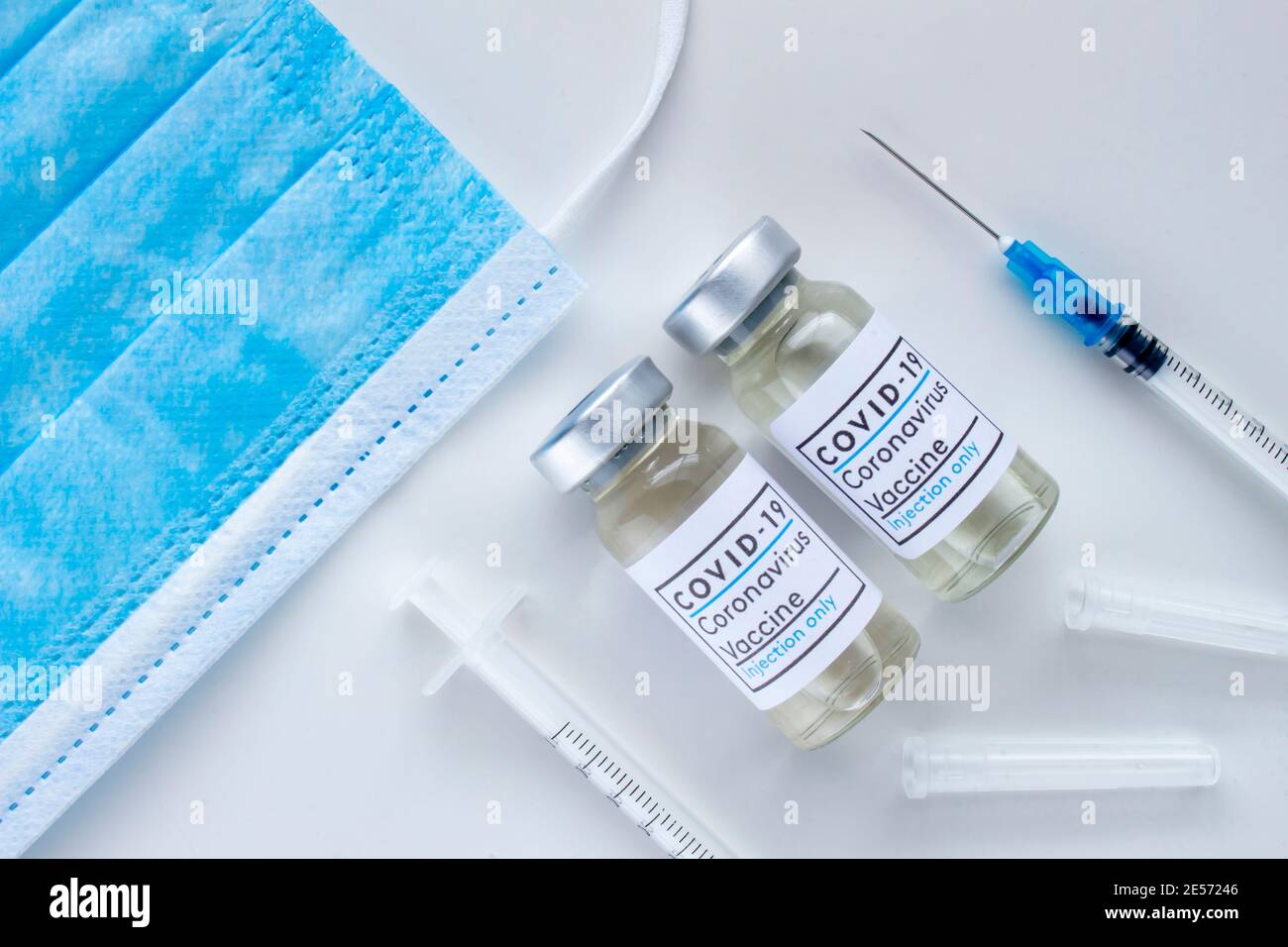 Quelques flacons de vaccin Covid-19 avec seringues stériles et un masque sur fond blanc Banque D'Images