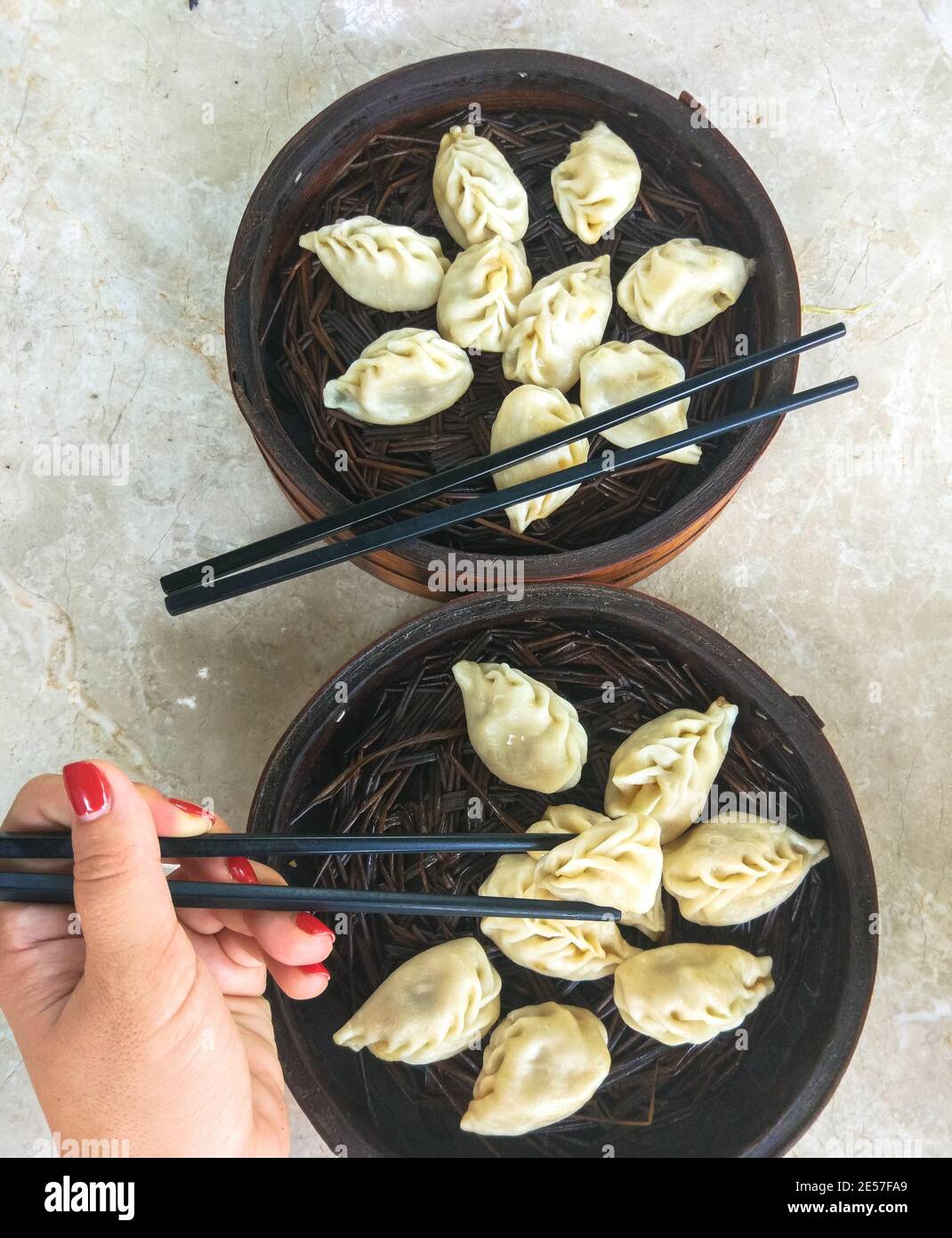 Femme tenant des baguettes, boulettes chinoises dans un panier vapeur, gros plan dim sum plat sur la table en marbre, cuisine chinoise traditionnelle Banque D'Images