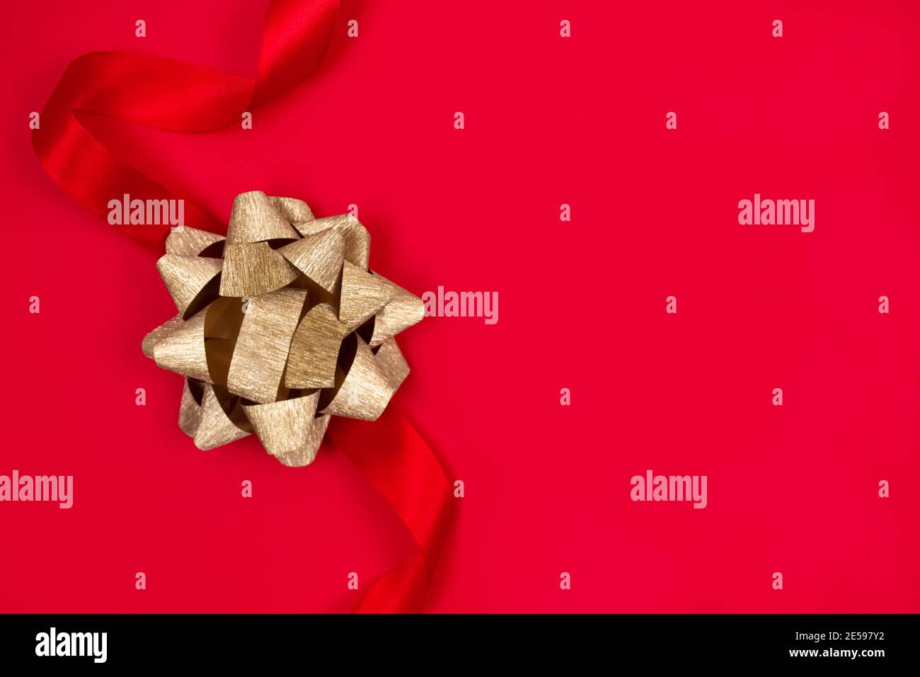Vue de dessus sur un noeud décoratif en ruban doré sur fond rouge avec espace pour le texte. Donner présente concept. Carte de vœux ou solde des fêtes Banque D'Images