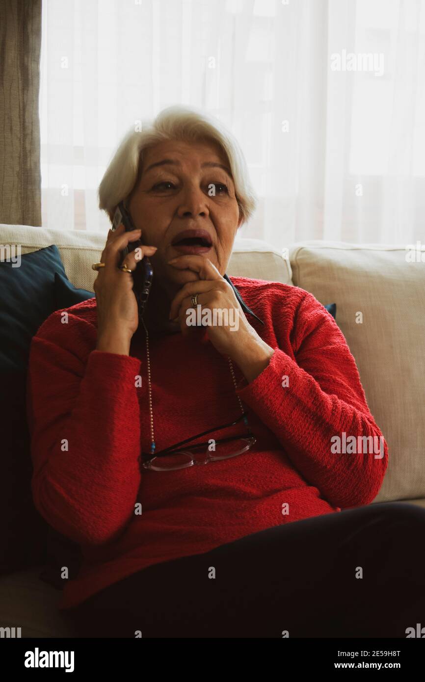 femme en chandail rouge assis sur un canapé blanc, a eu de mauvaises nouvelles au téléphone Banque D'Images