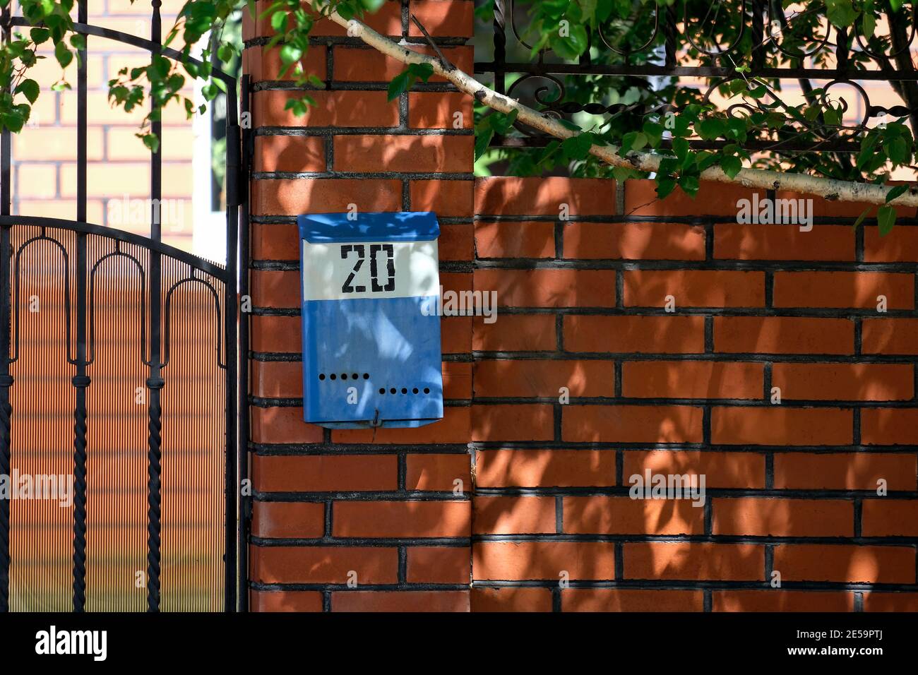Une boîte aux lettres bleue est suspendue sur la clôture. Numéro 20. La brique rouge et le bouleau sont visibles. Banque D'Images