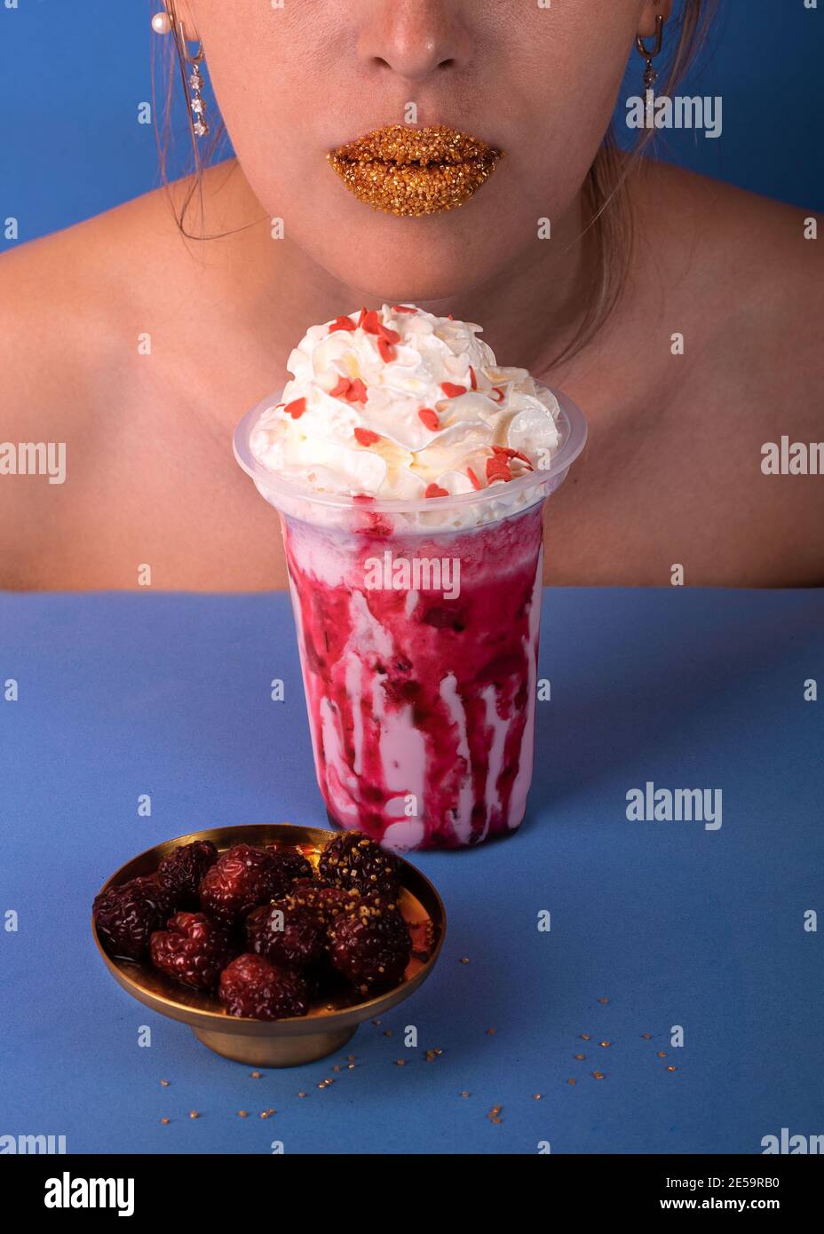 La jeune fille inhale l'arôme d'un milkshake à la framboise. En attendant un délicieux en-cas avec un beignet et un cocktail Banque D'Images