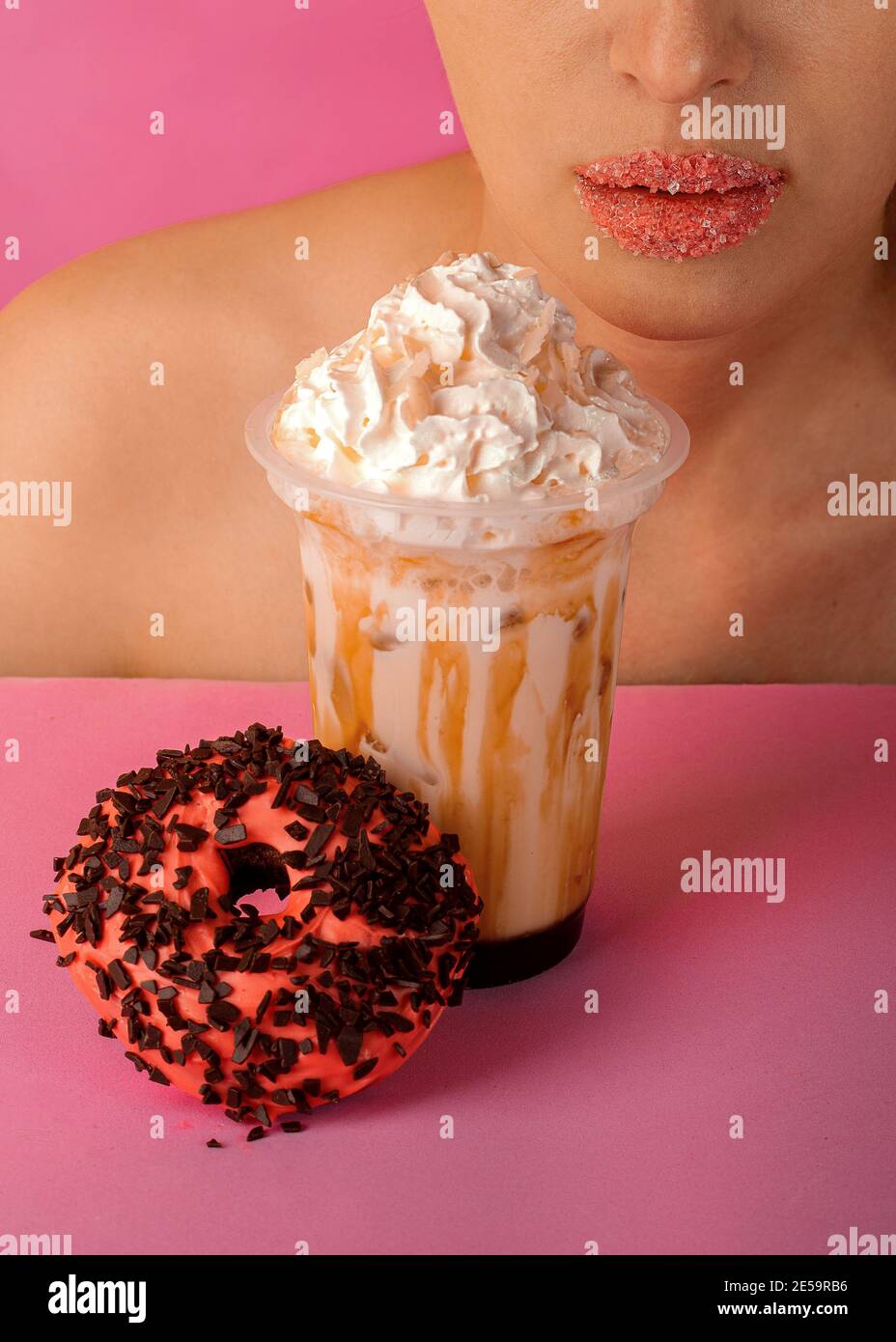 Une belle fille est sur le point de boire un milkshake au caramel avec un beignet sur fond rose. Belles lèvres Banque D'Images