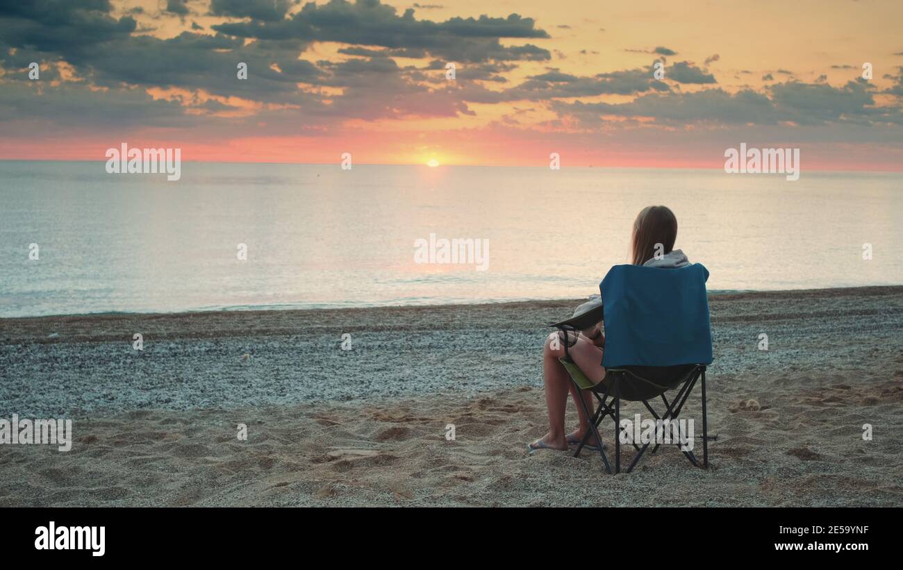 Femme admirant le coucher du soleil sur la mer assis dans une chaise de touriste pliante. Détente et plaisir de la nature. Banque D'Images