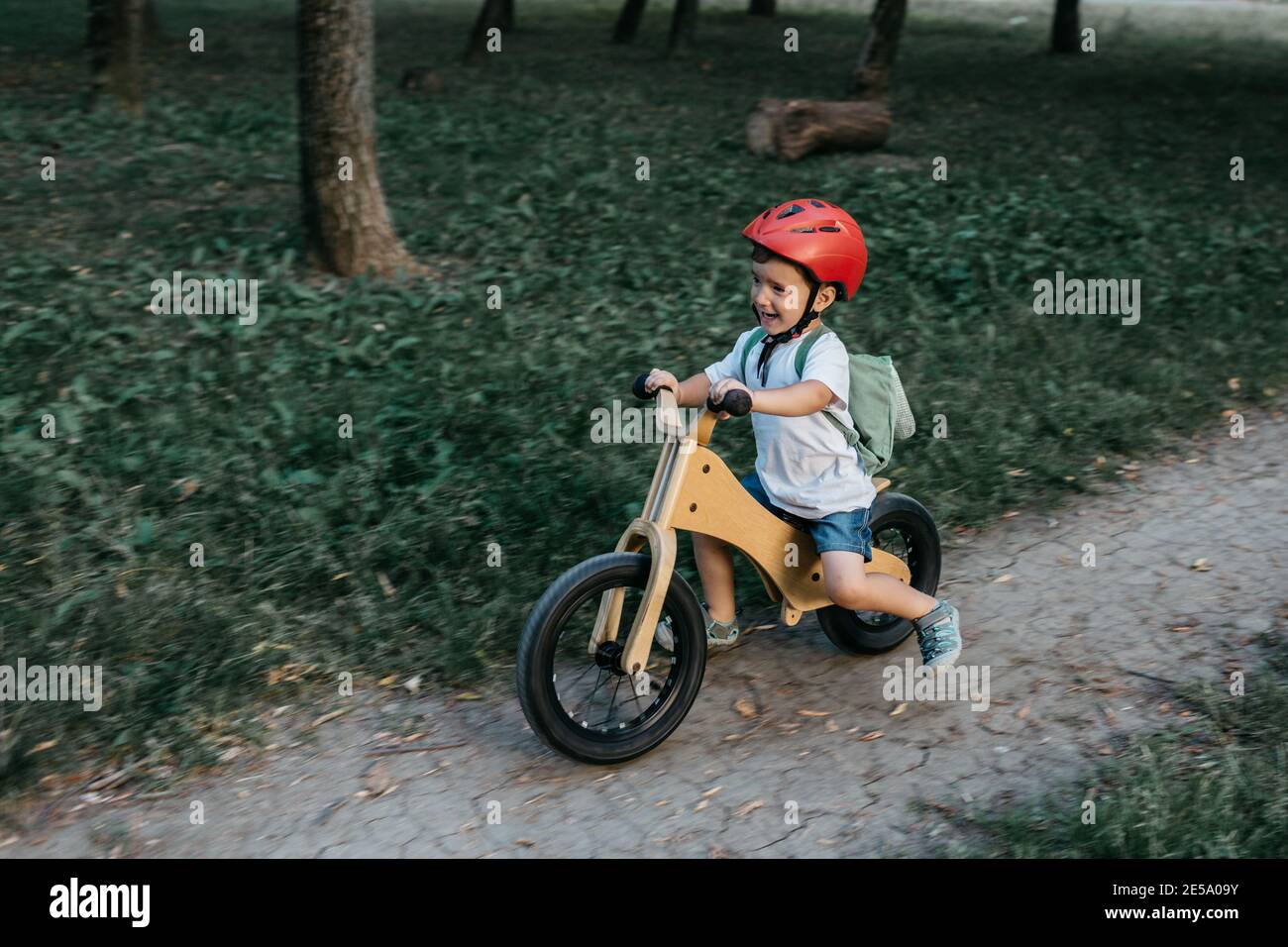 Enfant heureux portant un casque de vélo. Un jeune garçon souriant qui fait du vélo d'équilibre dans un parc en soirée d'été. Banque D'Images