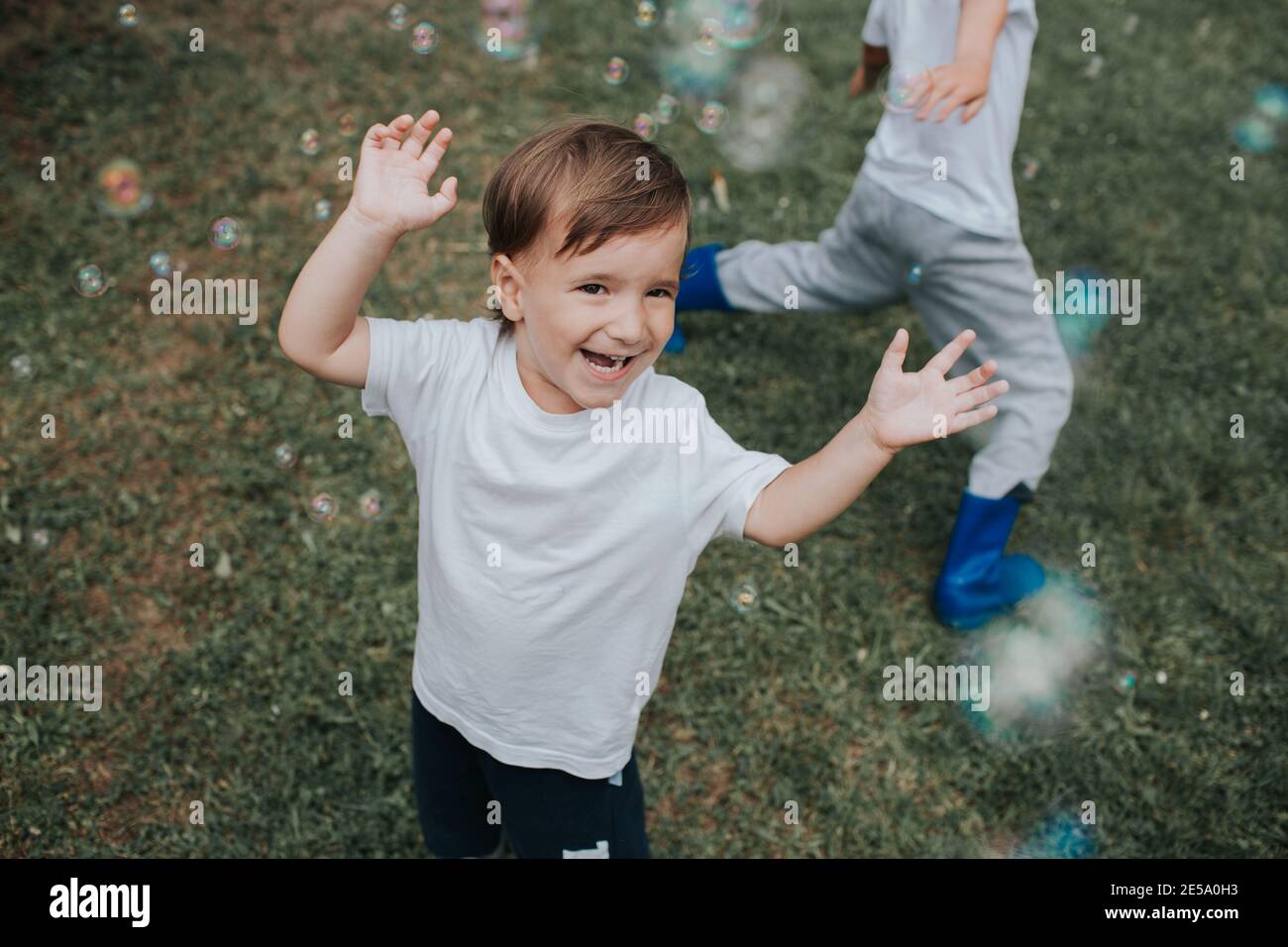 Garçon joyeux qui court après des bulles de savon. Un enfant heureux pourchassant des bulles de savon dehors dans un jardin, un jour d'été. Banque D'Images