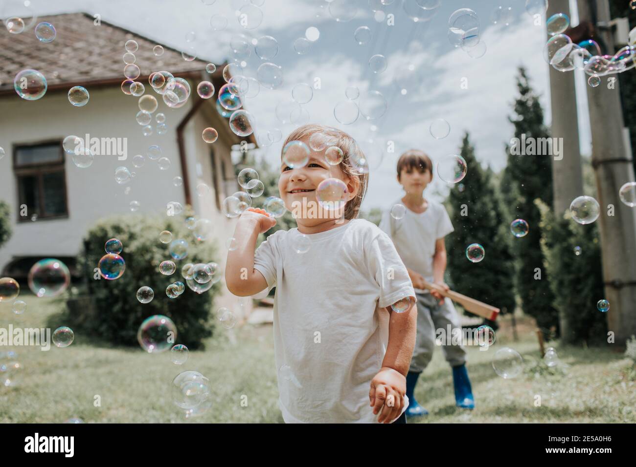 Garçon joyeux essayant de attraper des bulles de savon. Les enfants chassent les bulles de savon à l'extérieur dans un jardin par jour d'été. Banque D'Images