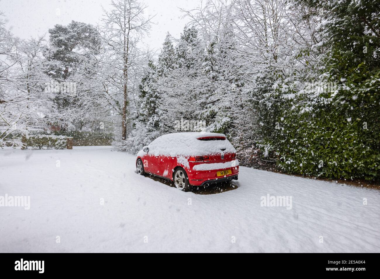 Une voiture rouge Volkswagen Golf GTI garée dans un périurbain couvert de neige pendant une forte chute de neige en hiver : Woking, Surrey, sud-est de l'Angleterre Banque D'Images
