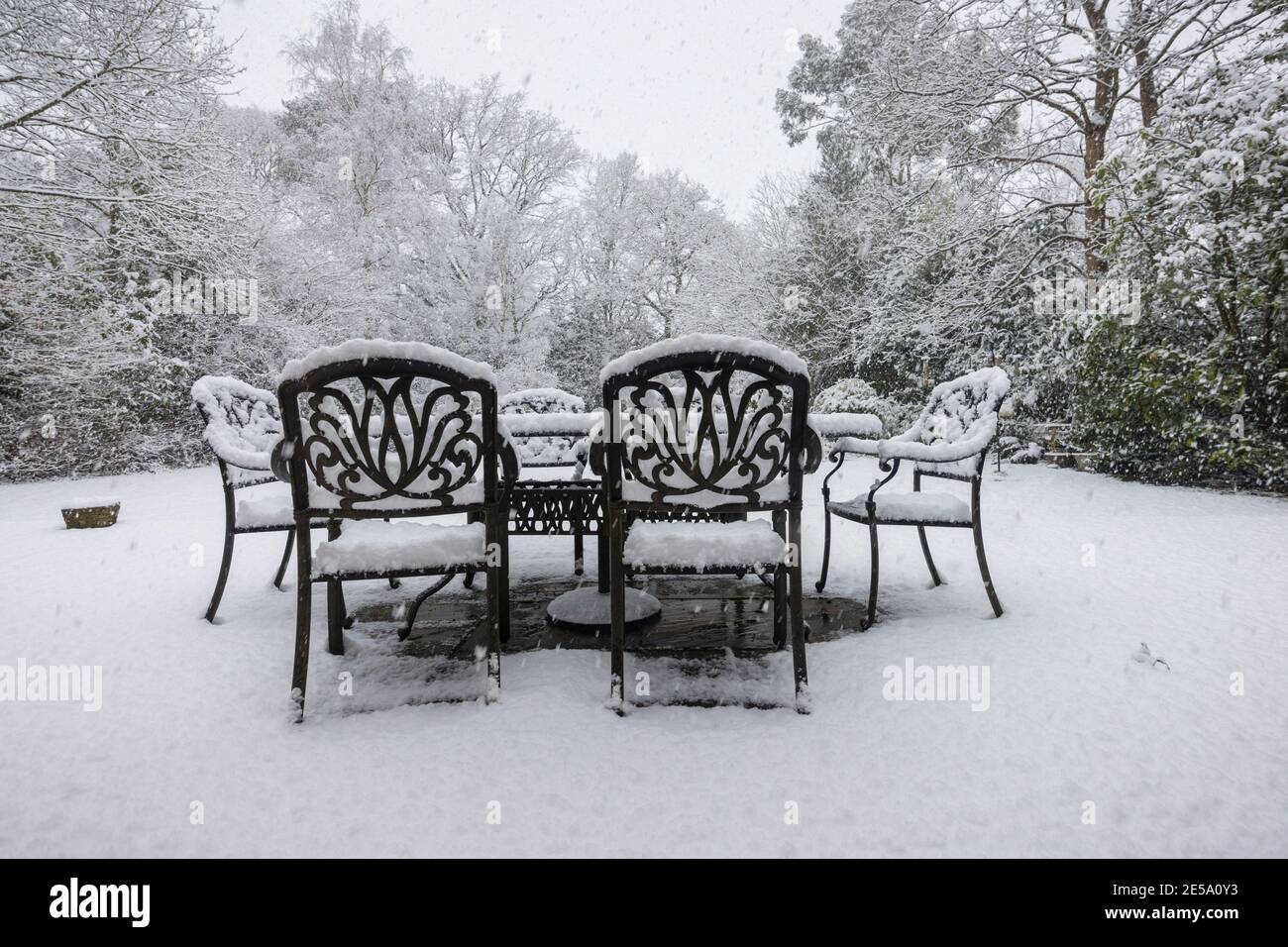 Tables et chaises extérieures sur un patio et arbres couverts de neige lors d'une forte chute de neige dans un jardin de banlieue Woking, Surrey, au sud-est de l'Angleterre Banque D'Images
