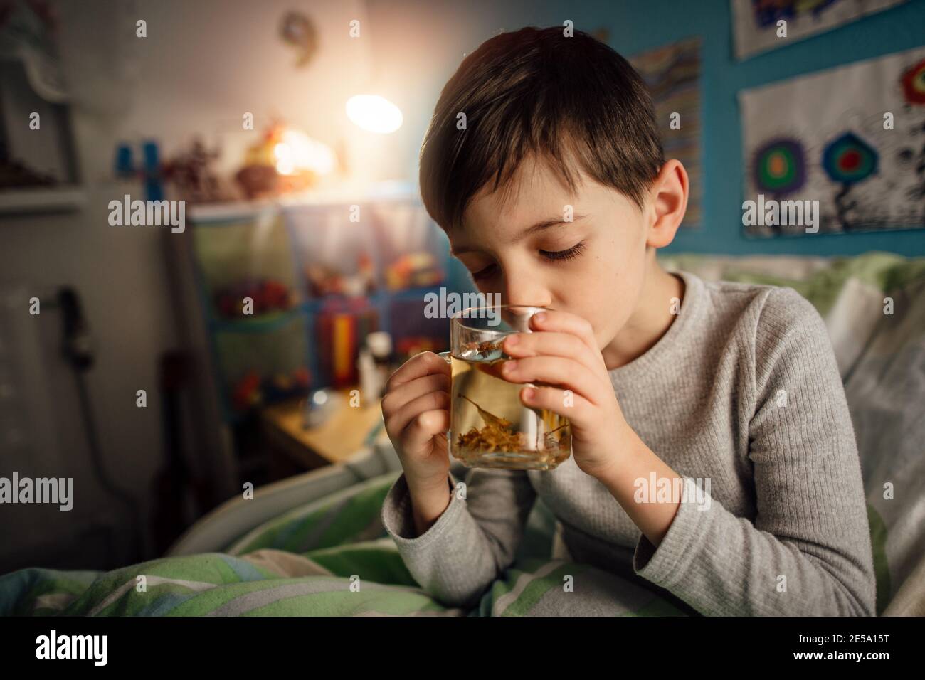 Un portrait d'un enfant avec une tisane froide dans son lit. Un jeune garçon avec le conduit de fumée sirotant une boisson chaude dans sa chambre la nuit. Banque D'Images