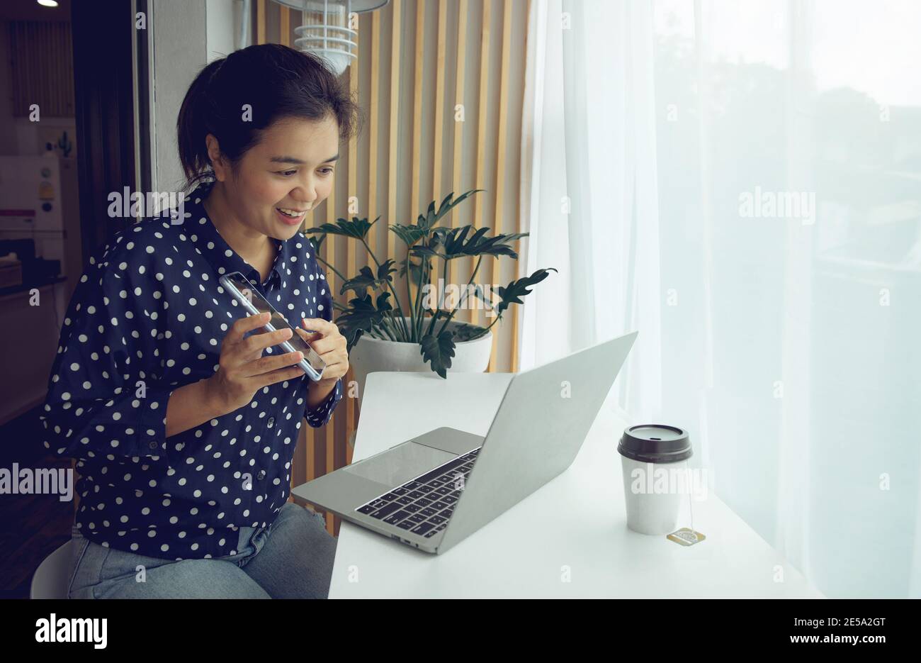 Femme d'affaires ayant un appel de conférence par ordinateur portable et téléphone. Bureau à domicile. Rester à la maison et travailler de la maison concept pendant la pandémie de coronavirus. Banque D'Images